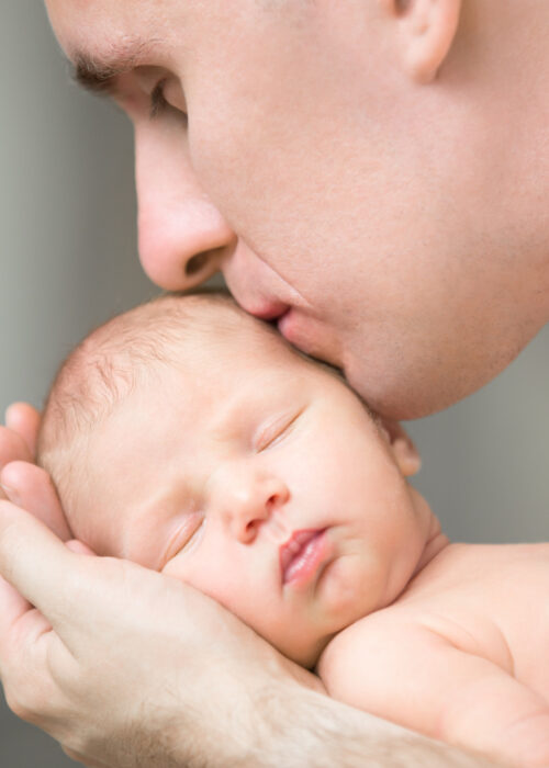 Young,Man,Kissing,A,Newborn,,He,Holds,Gently,In,His
