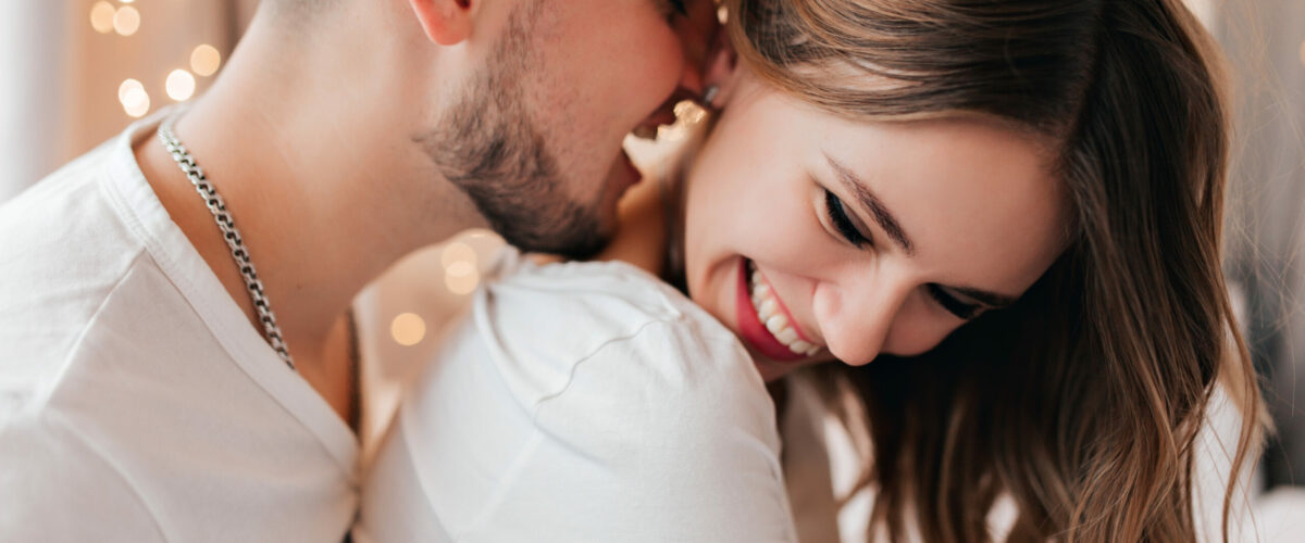 White,Young,Woman,Laughing,While,Husband,Kissing,Her,Neck.,Indoor